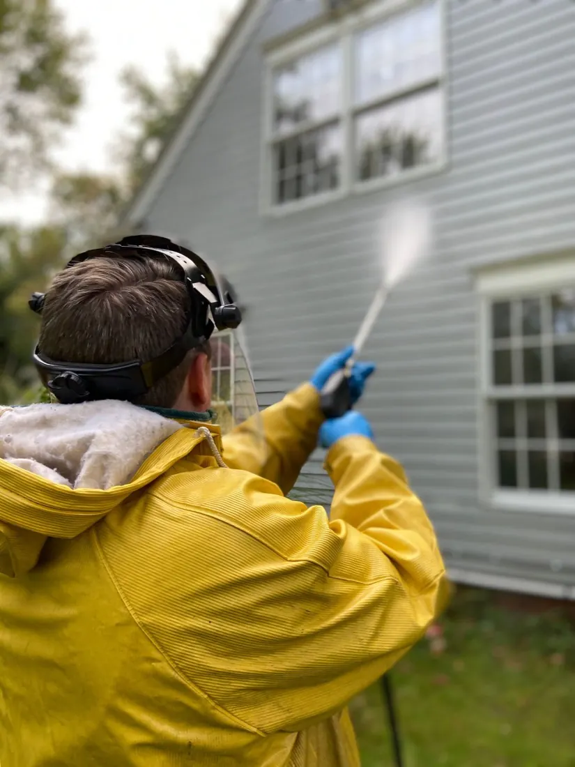 Nettoyage d'une façade au nettoyeur basse pression par un opérateur équipé d'une visière.