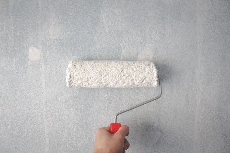 Rouleau de peinture appliquant une peinture claire sur un mur extérieur texturé.