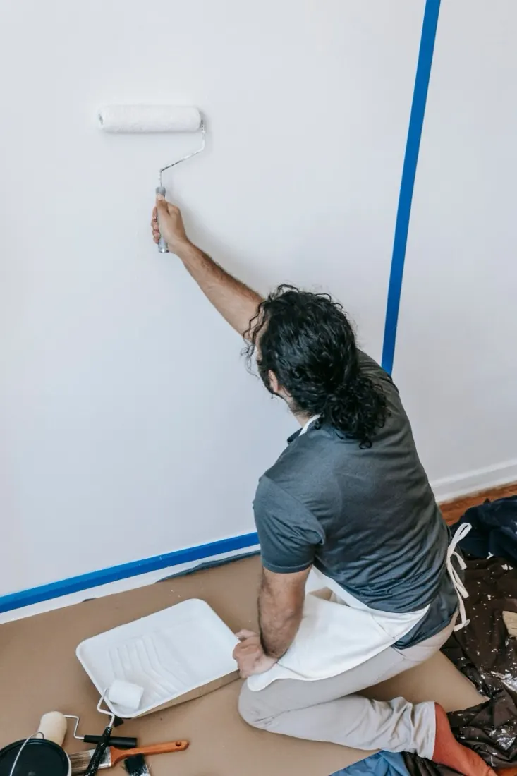 Peintre appliquant une peinture blanche au rouleau sur un mur intérieur préparé.